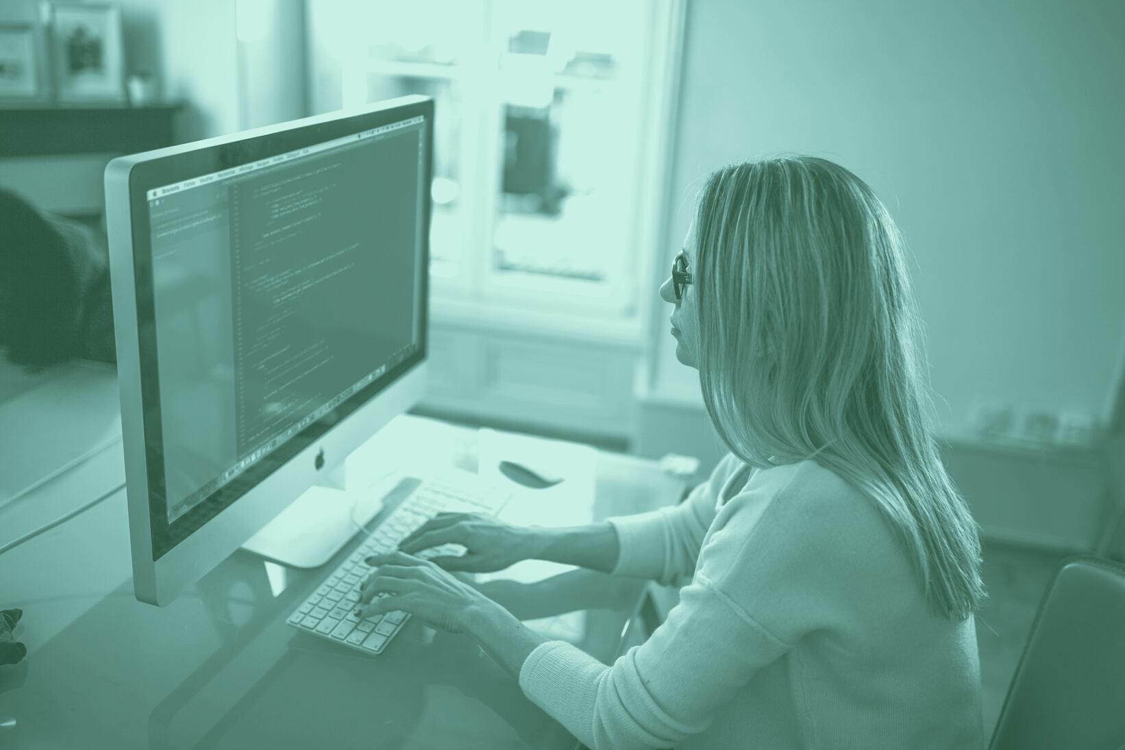 Seated Woman Typing on Apple Mighty Keyboard in Front of Turned-on Silver Imac